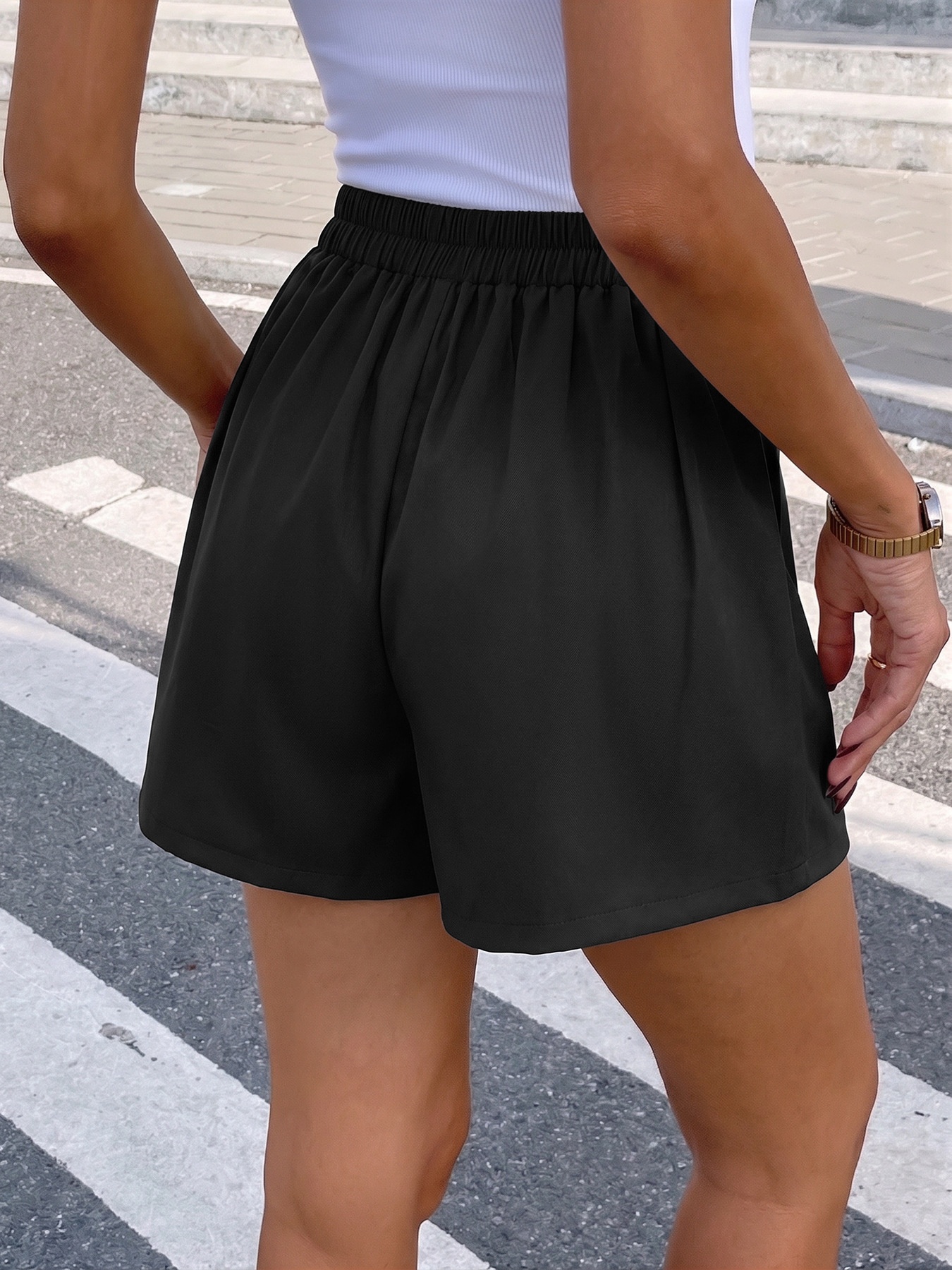 Eleganti shorts neri a vita alta con pieghe e bottone a rosa.