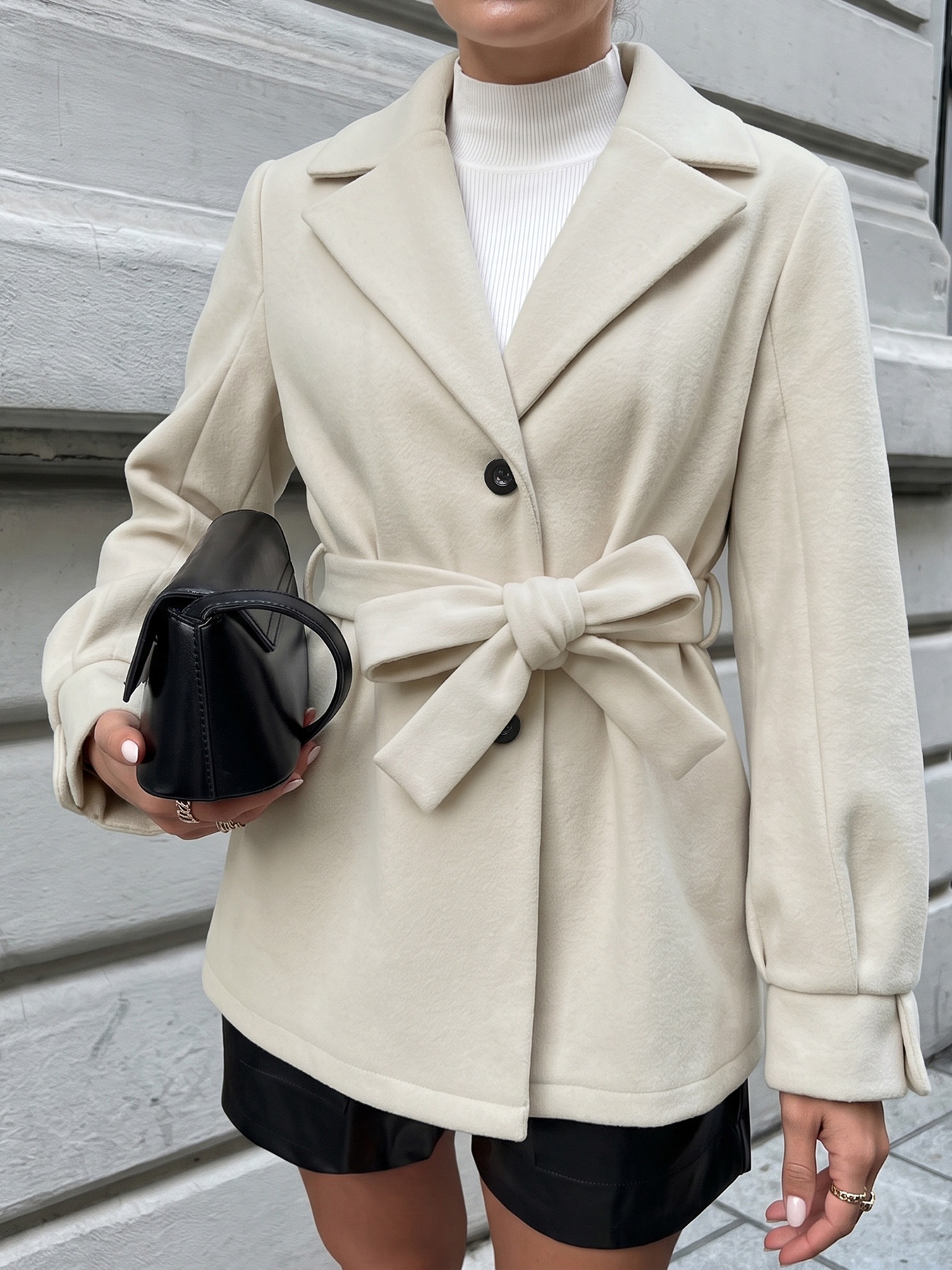 Cappotto beige con cintura e abbottonatura frontale, con colletto a revers.