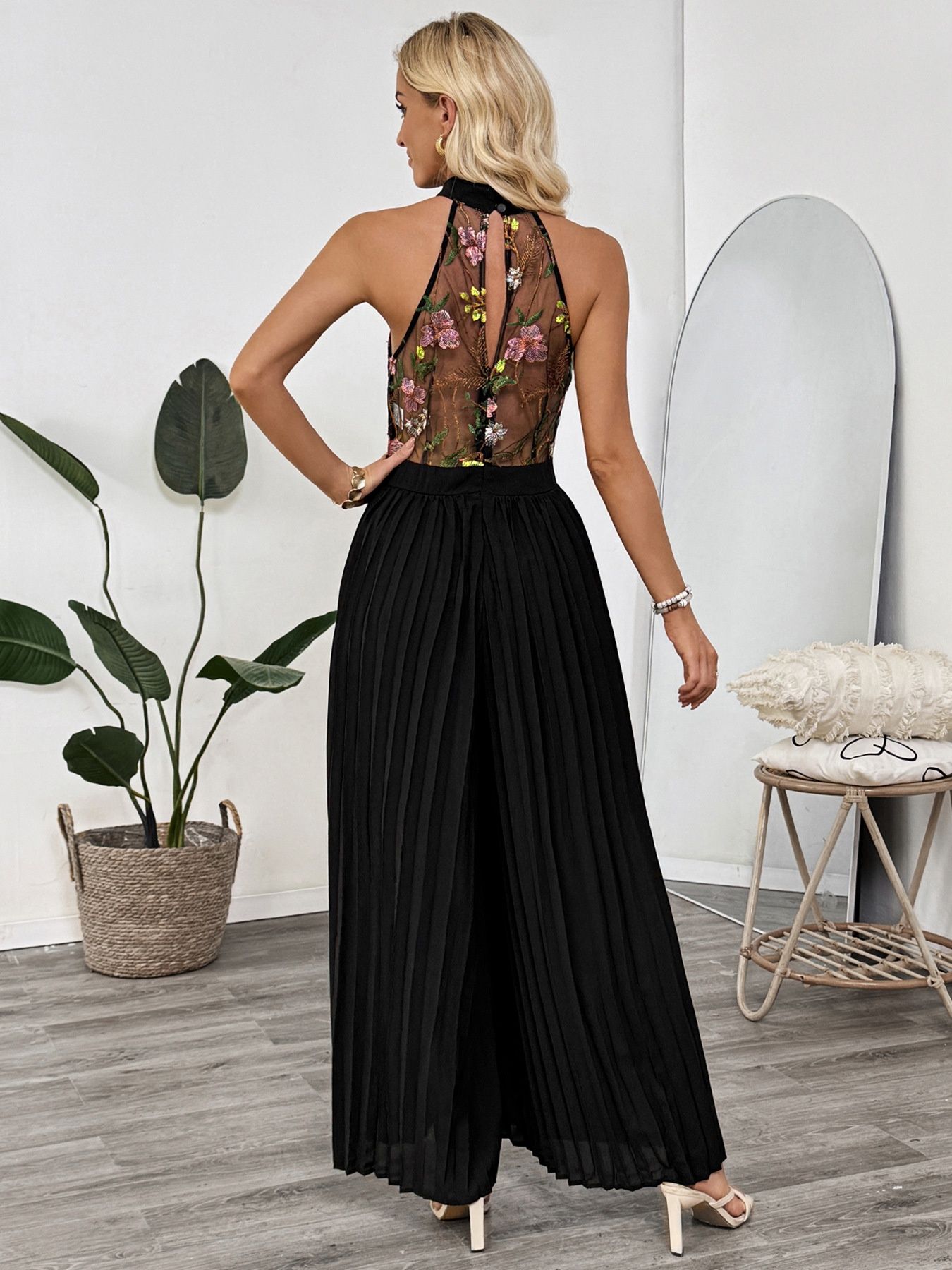 Mono negro con estampado floral, escote halter y pernera ancha plisada.