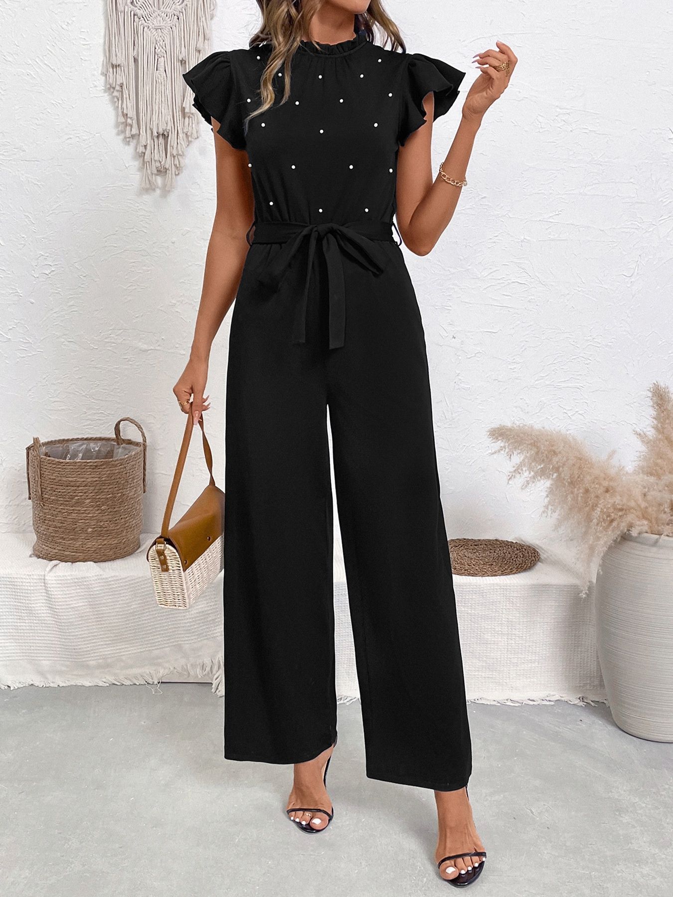 Mono negro con volantes en las mangas y cinturón, adornado con perlas.