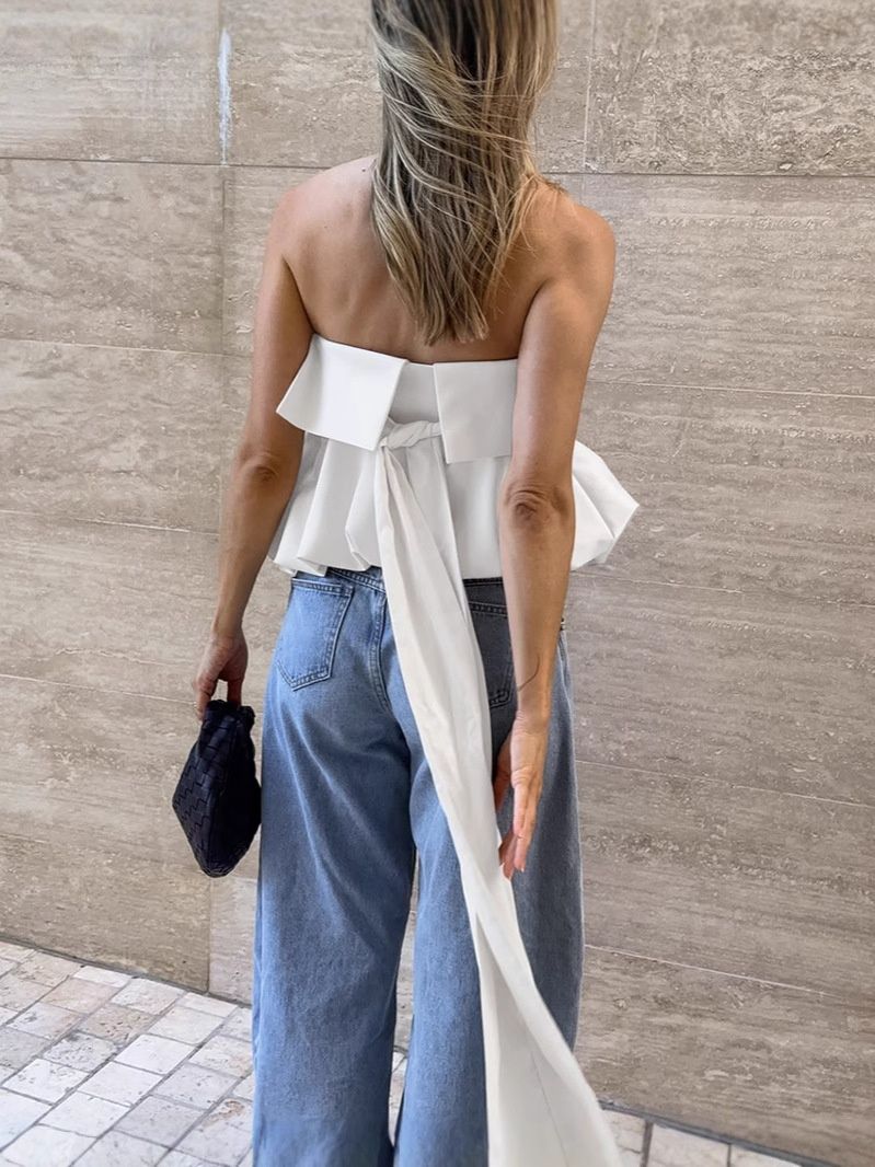 Top blanco sin tirantes con bajo abullonado y lazo largo en la espalda.