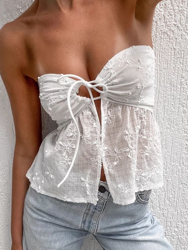 Top blanco sin tirantes con bordado floral y lazo frontal.