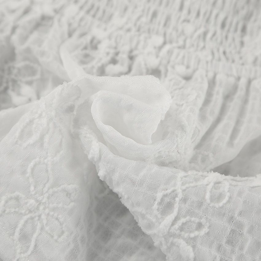 Top blanco sin tirantes con bordado floral y lazo frontal.