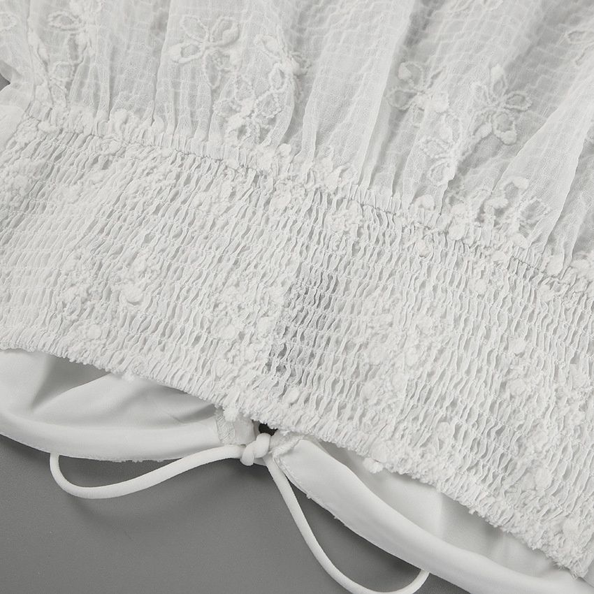 Top blanco sin tirantes con bordado floral y lazo frontal.