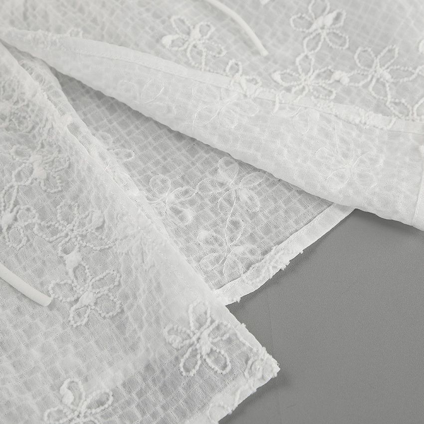 Top blanco sin tirantes con bordado floral y lazo frontal.