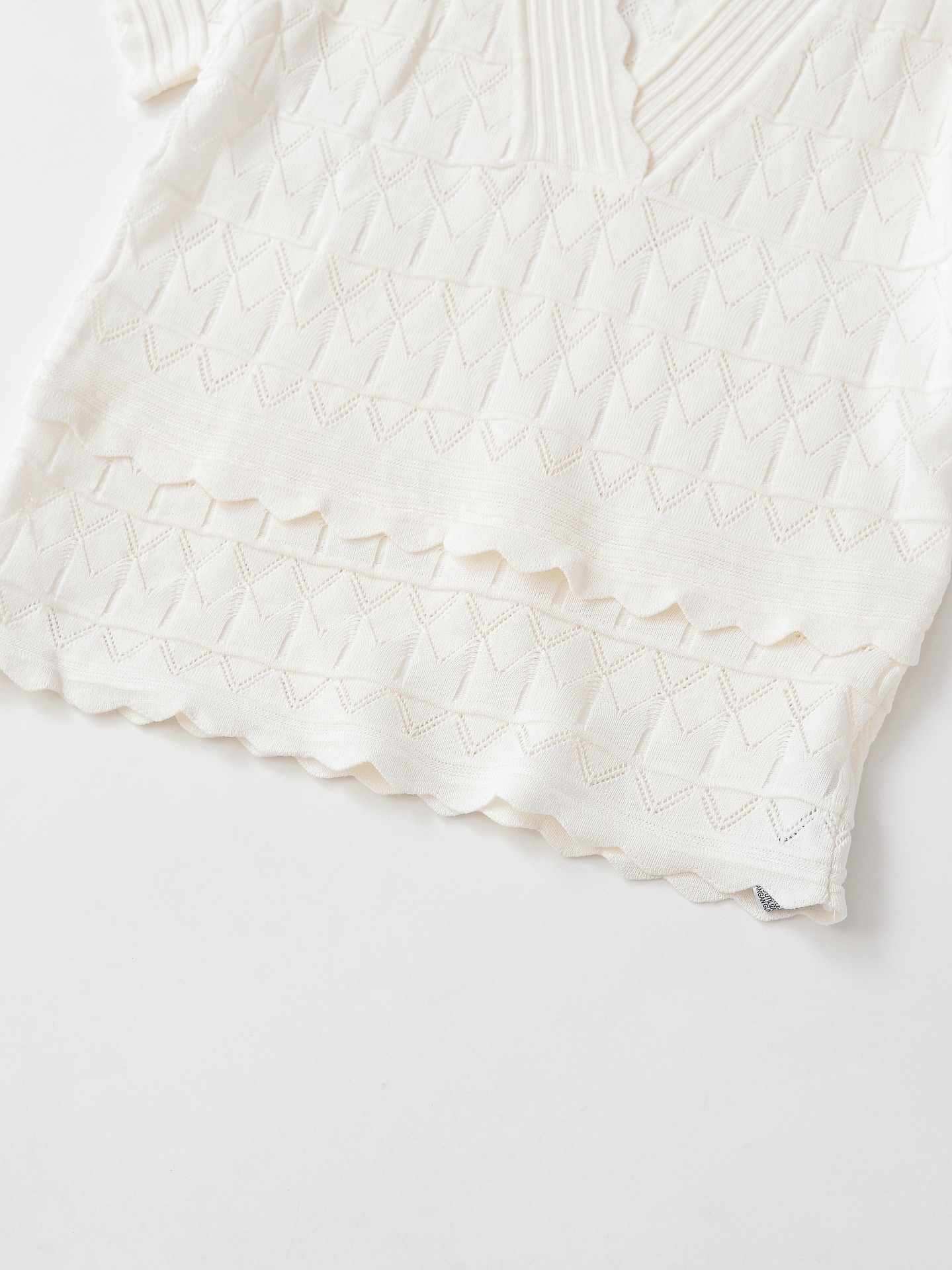 Elegante top a maniche corte con scollo a V e orlo smerlato, in maglia traforata.