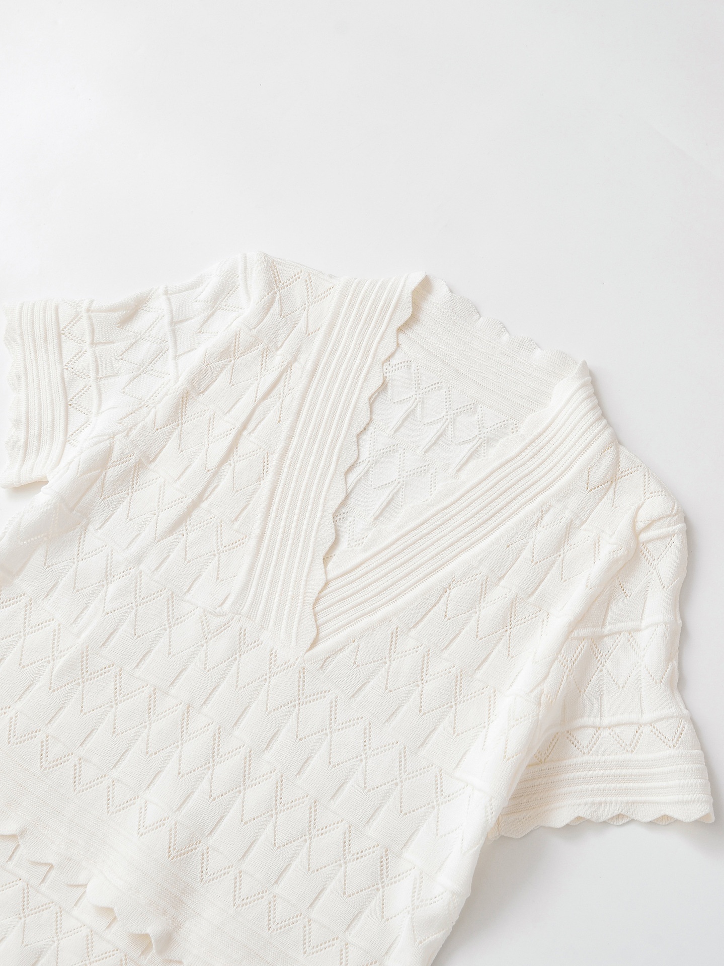 Elegante top a maniche corte con scollo a V e orlo smerlato, in maglia traforata.